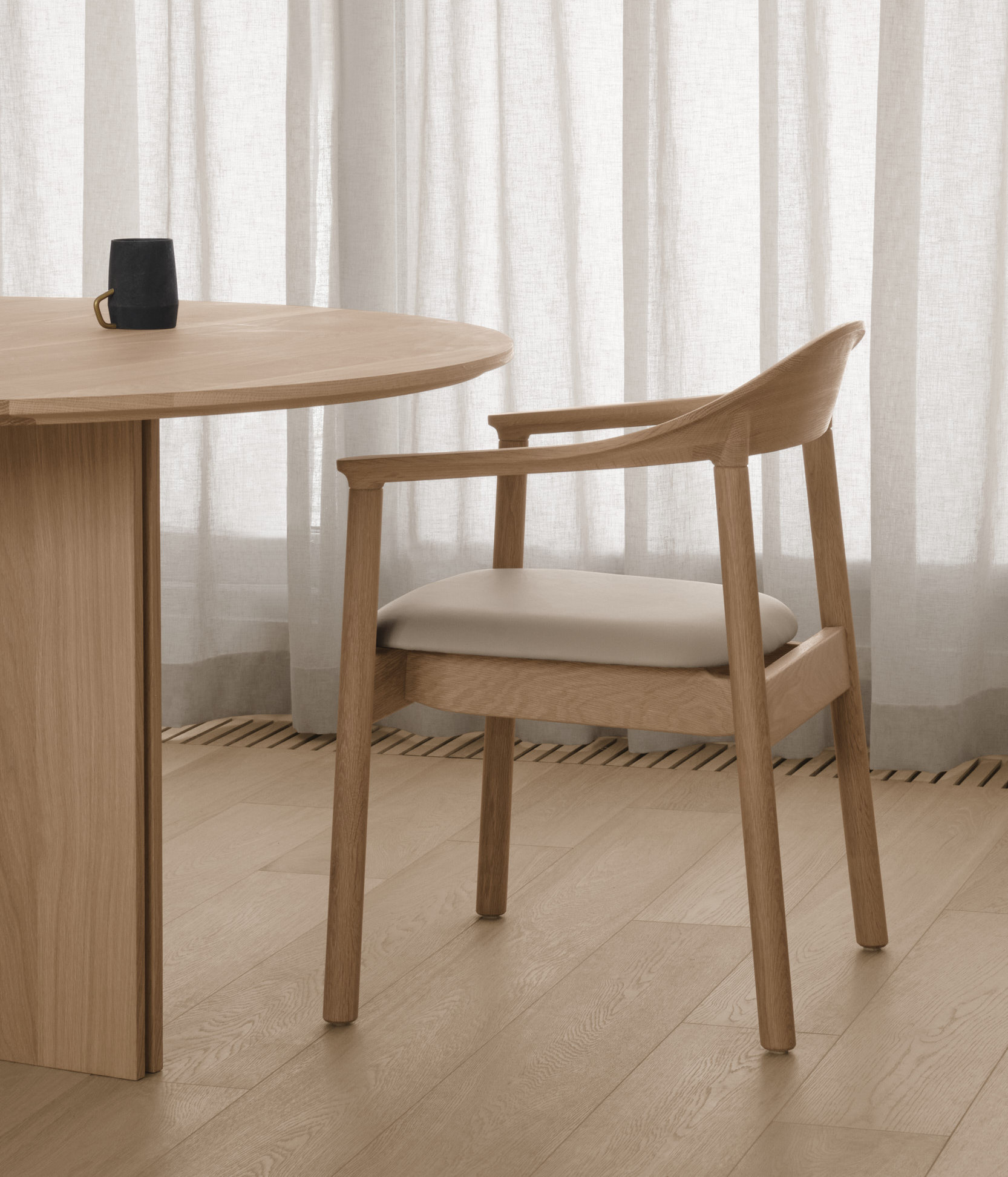 A Dune chair with armrests in cream and white oak in front of a cream coloured curtain