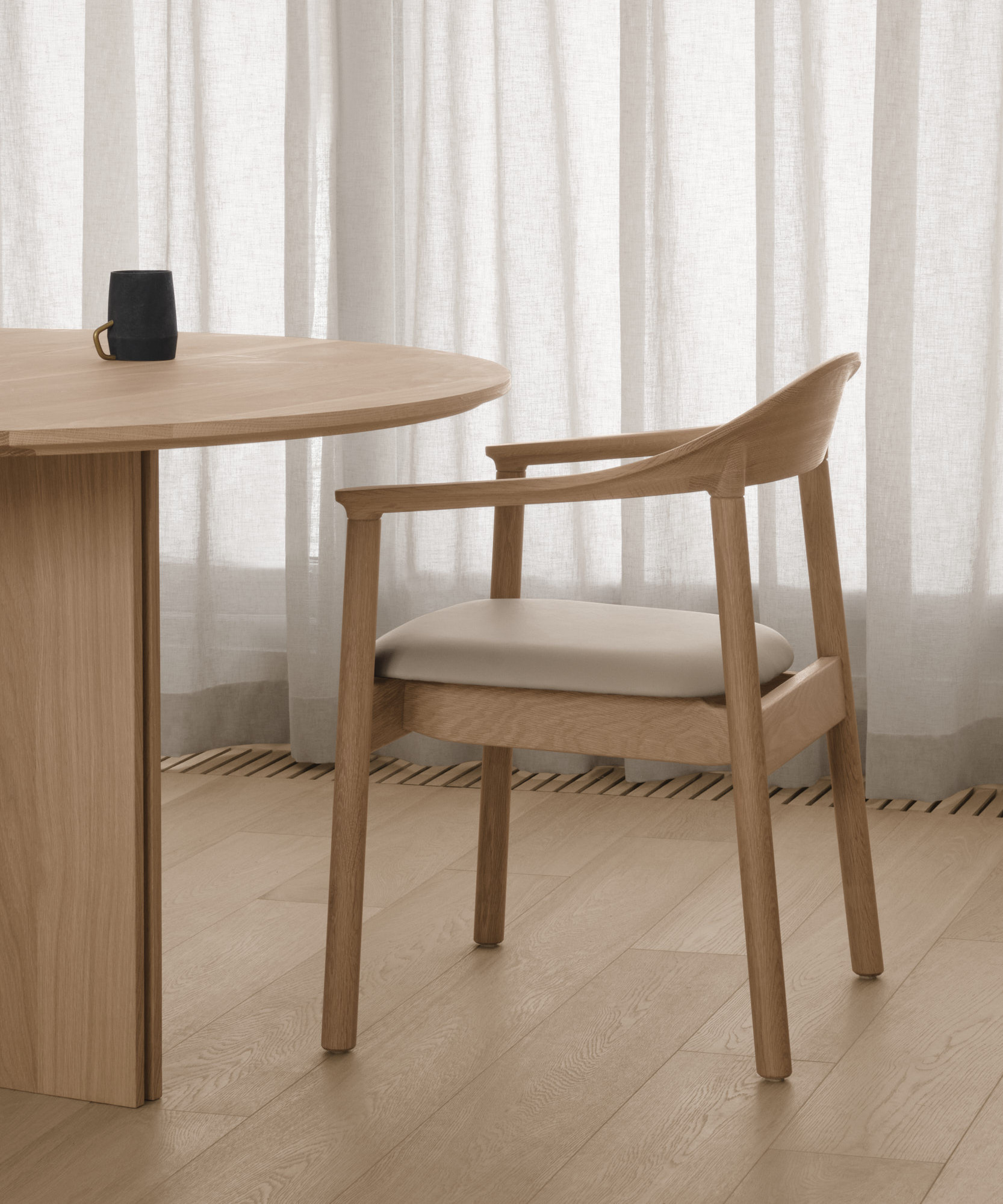 A Dune chair with armrests in cream and white oak in front of a cream coloured curtain