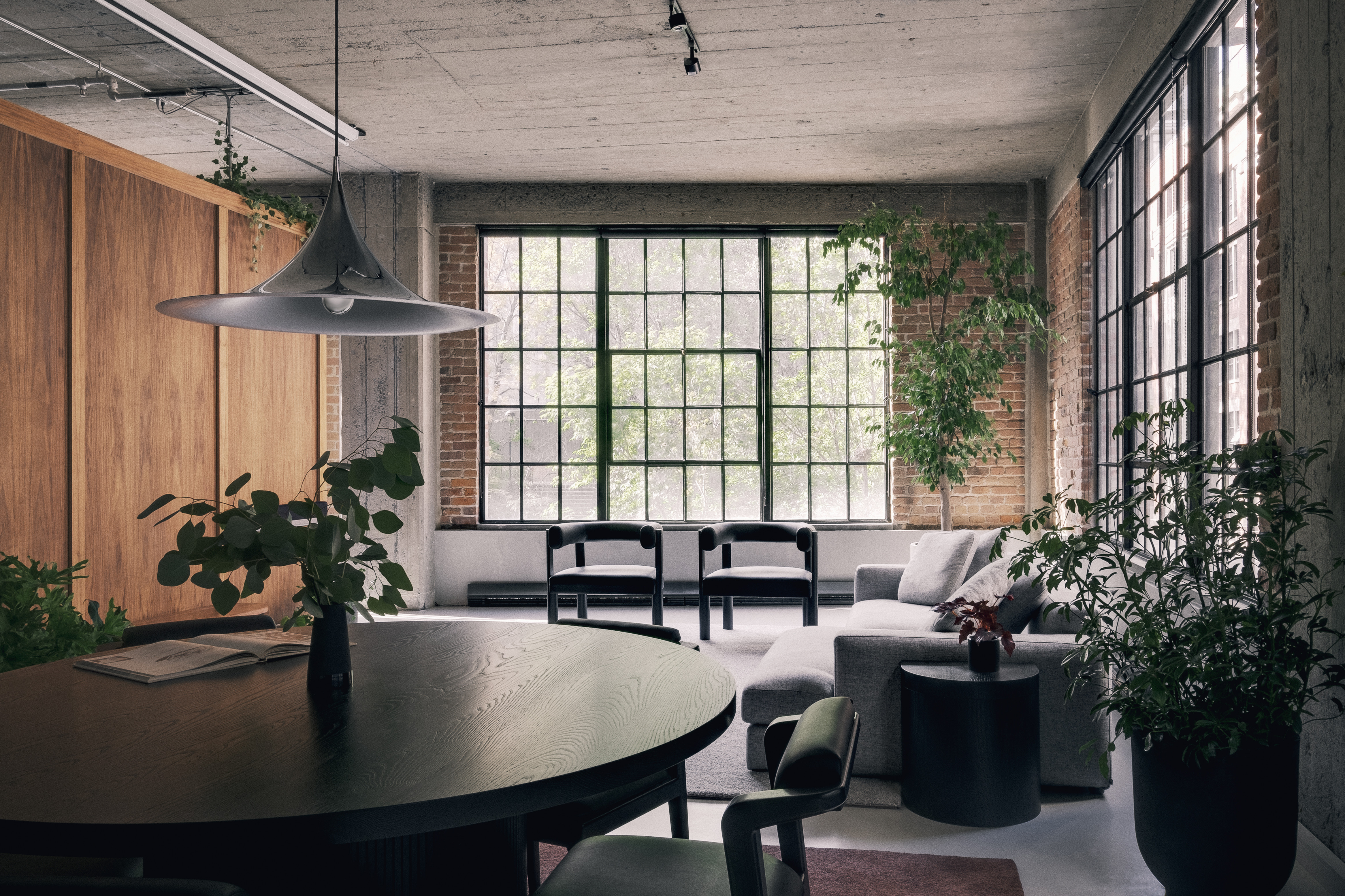 a wide shot view of a custom table with Nord chairs, a living area with cove chairs a couch and a cache in an industrial style loft