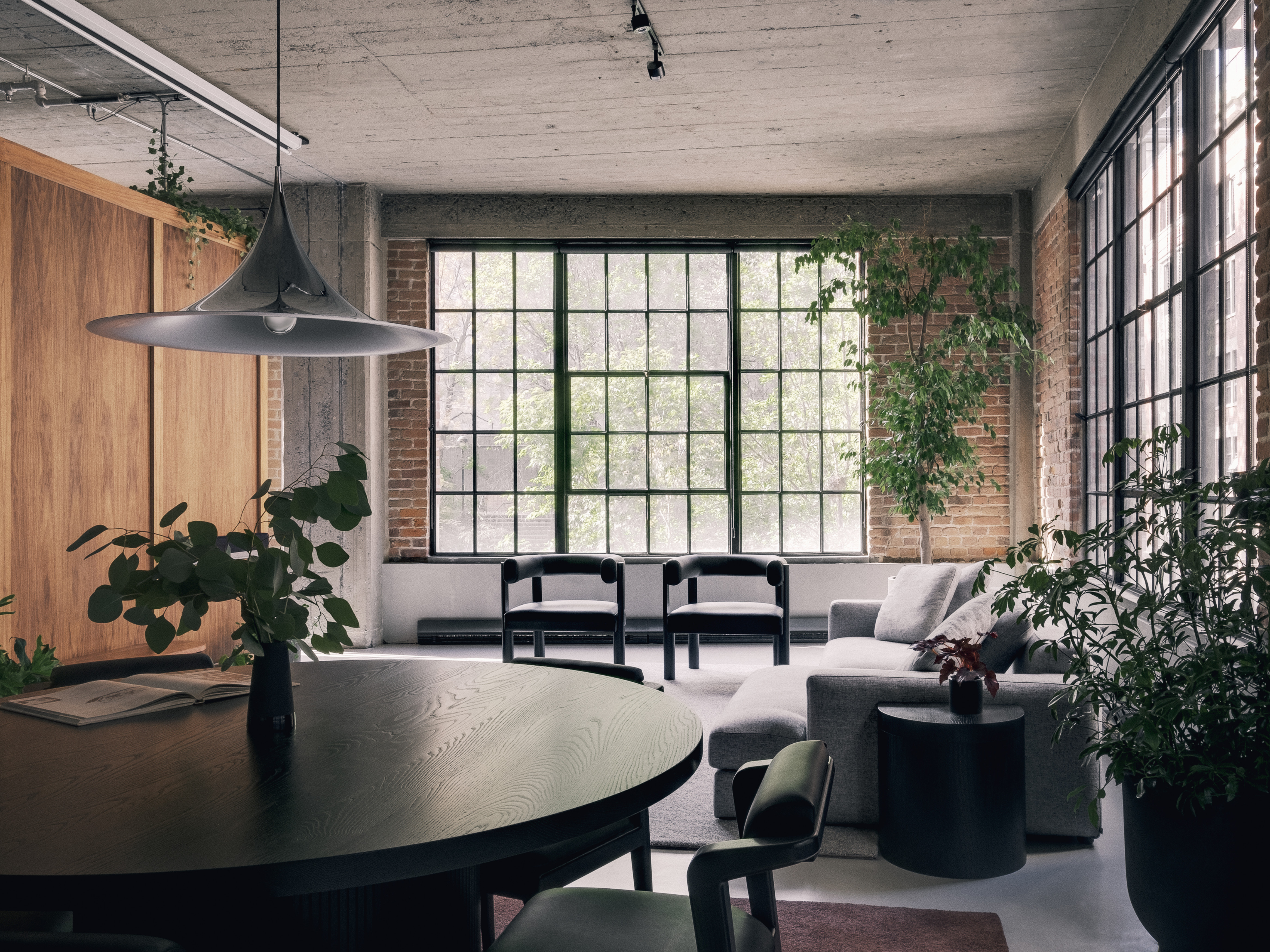 a wide shot view of a custom table with Nord chairs, a living area with cove chairs a couch and a cache in an industrial style loft